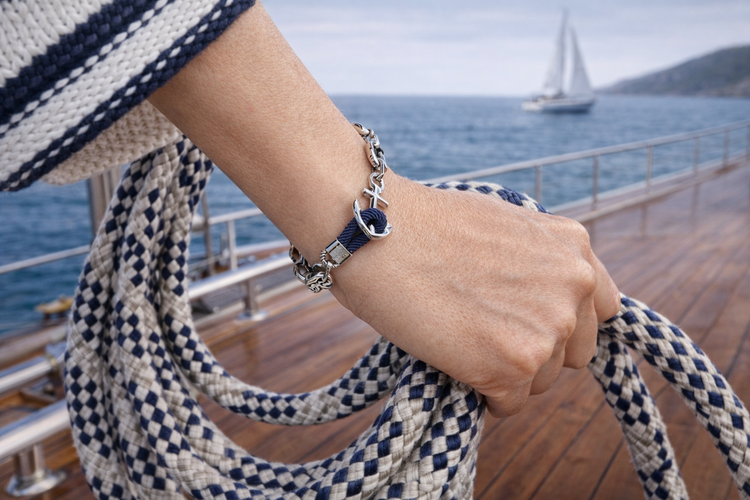 Silver anchor bracelet on navy rope, worn on a wrist aboard a boat at sea
